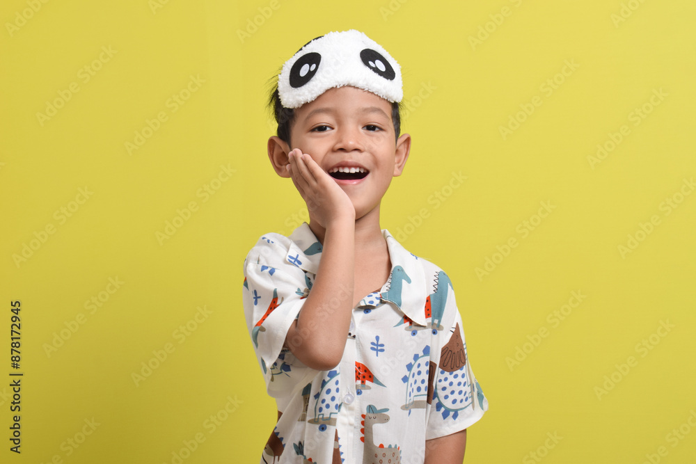 Portrait of Cute Asian child wearing pajamas and sleep mask isolated on yellow background. Healthy sleep concept. Copy space Portrait of Cute Asian child wearing pajamas and sleep mask isolated on yellow background. Healthy sleep concept. Copy space