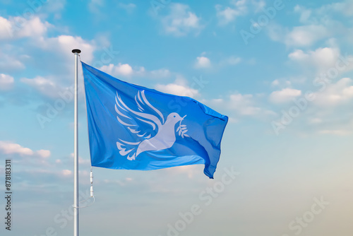 Waving blue peace flag with white dove holding an olive branch.in front of a moody blue sky photo