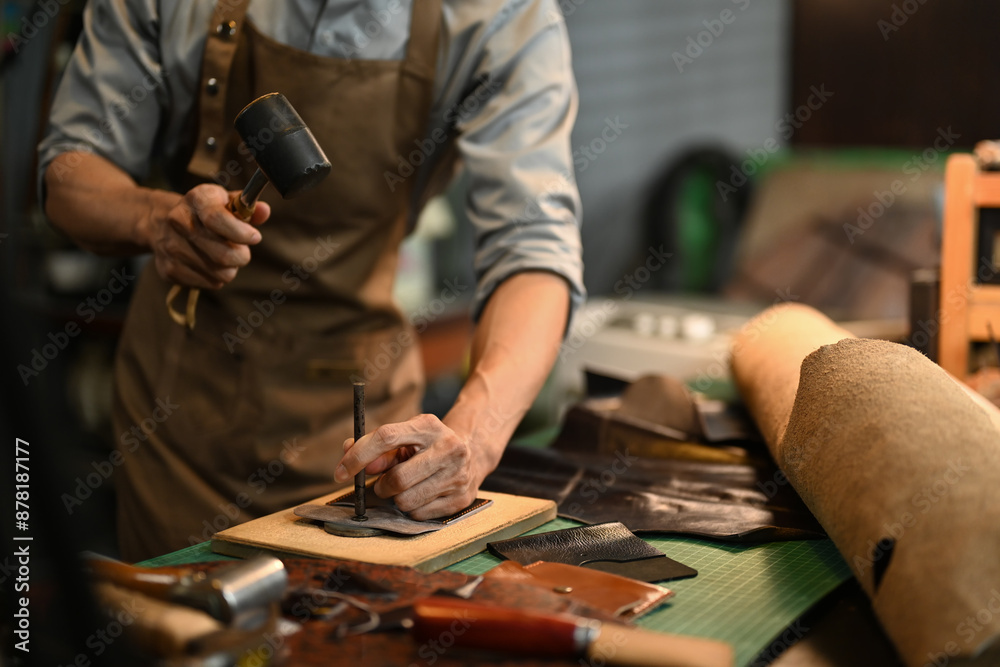 Obraz premium Cropped shot male artisan punching holes in leather piece. Small business and handmade concept
