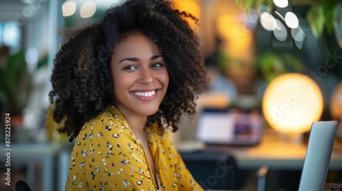 Joyful young woman smiling while working on a laptop in the office.