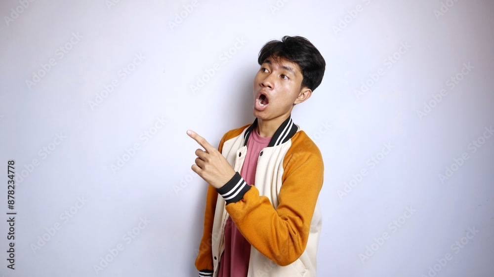 casual shocked young handsome Asian man wearing a jacket giving a gesture pointing upwards casual shocked young handsome Asian man wearing a jacket giving a gesture pointing upwards