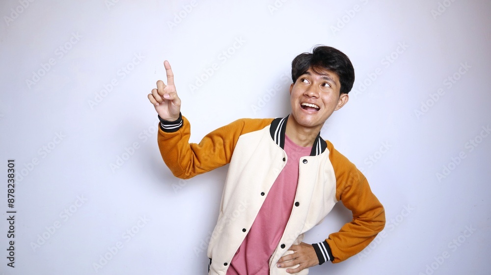 casual excited young handsome Asian man wearing a jacket giving a gesture pointing upwards casual excited young handsome Asian man wearing a jacket giving a gesture pointing upwards