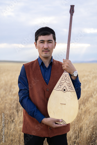 Kazakh, a man in Kazakh national dress playing dombra in the steppe. Kazakhstan. Central Asia. Nomads. | Казах, мужчина в казахской национальной одежде играет на домбре в степи. Казахстан.Средняя Азия photo