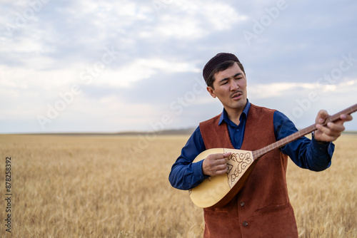 Kazakh, a man in Kazakh national dress playing dombra in the steppe. Kazakhstan. Central Asia. Nomads. | Казах, мужчина в казахской национальной одежде играет на домбре в степи. Казахстан.Средняя Азия photo