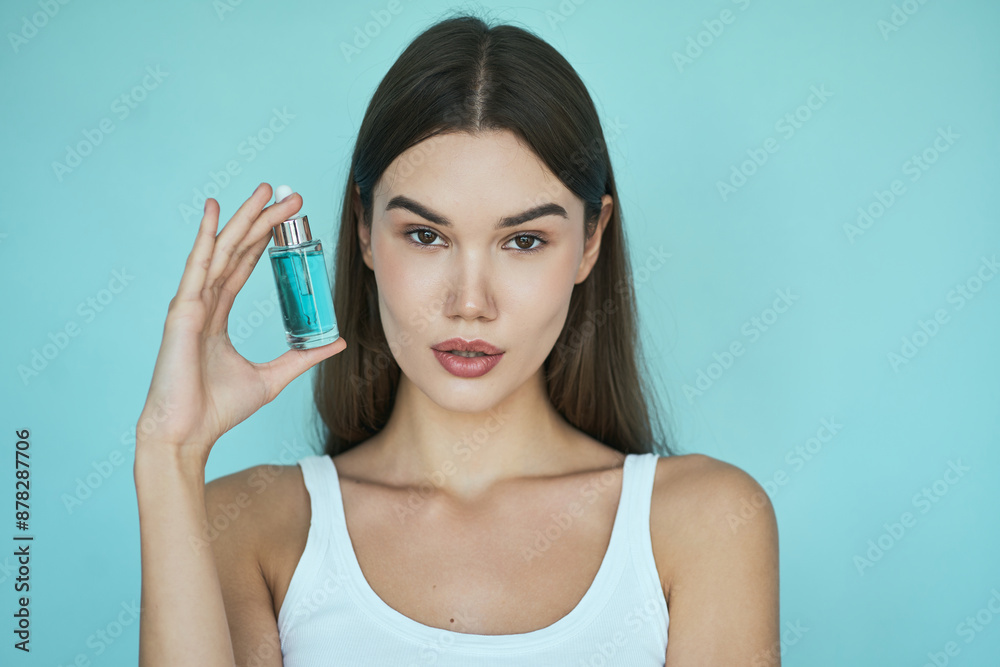 Woman Holding Serum Bottle For Skincare Against Light Blue Background. Concept Of Modern Cosmetics, Beauty Routine, And Skincare Products Woman Holding Serum Bottle For Skincare Against Light Blue Background. Concept Of Modern Cosmetics, Beauty Routine, And Skincare Products