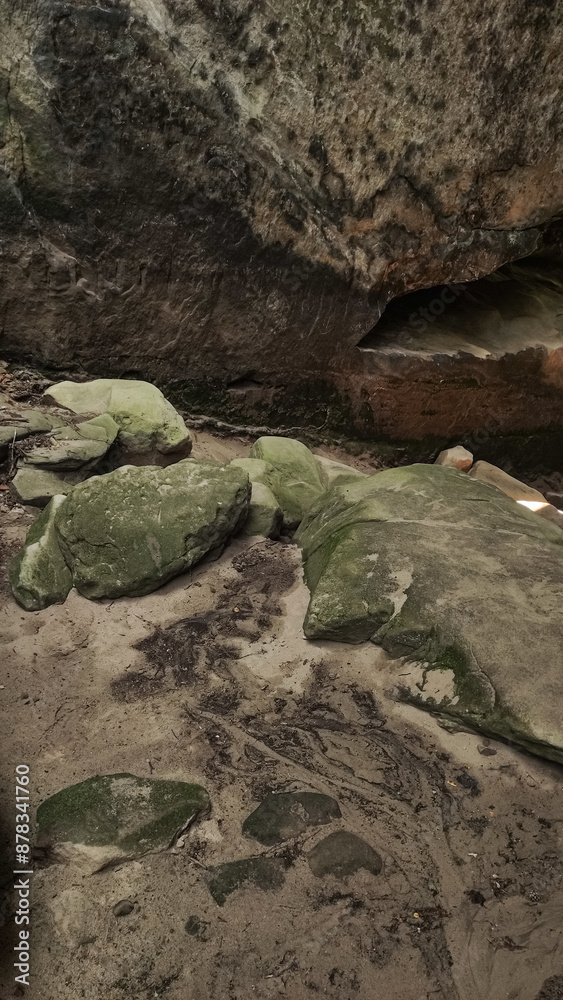 Large, moss-covered rocks sit beneath a sandstone overhang Large, moss-covered rocks sit beneath a sandstone overhang