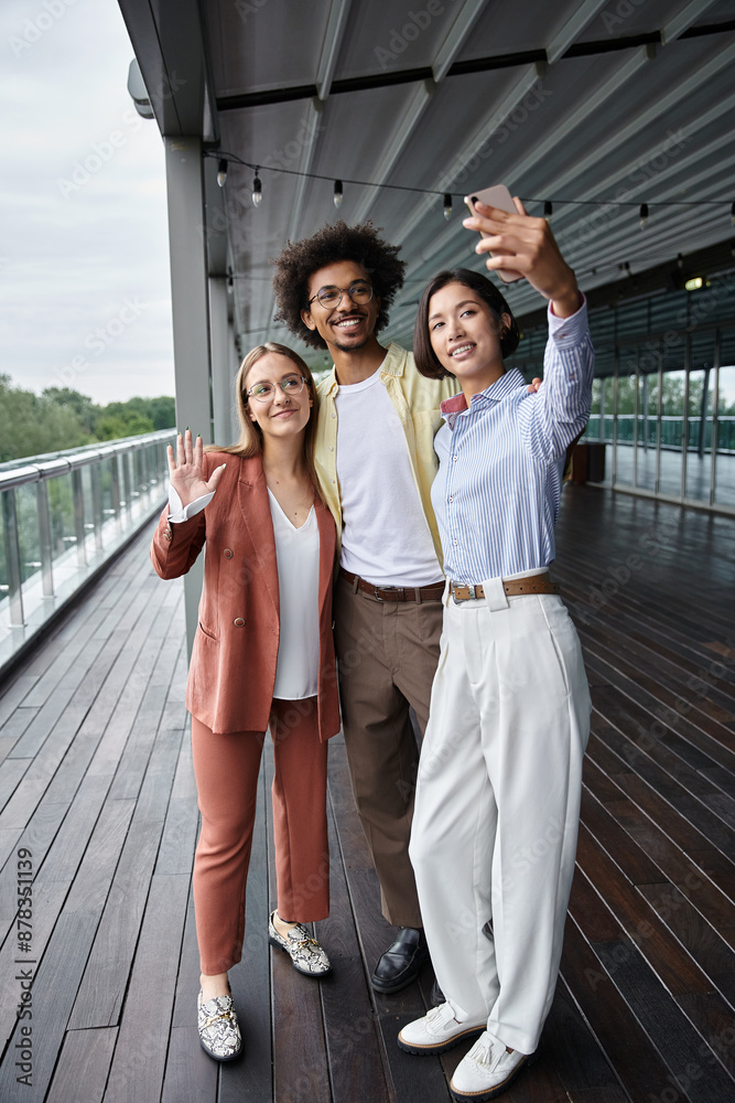 Obraz premium Three diverse coworkers enjoy a afternoon on a modern rooftop terrace, sharing laughs and taking a selfie.