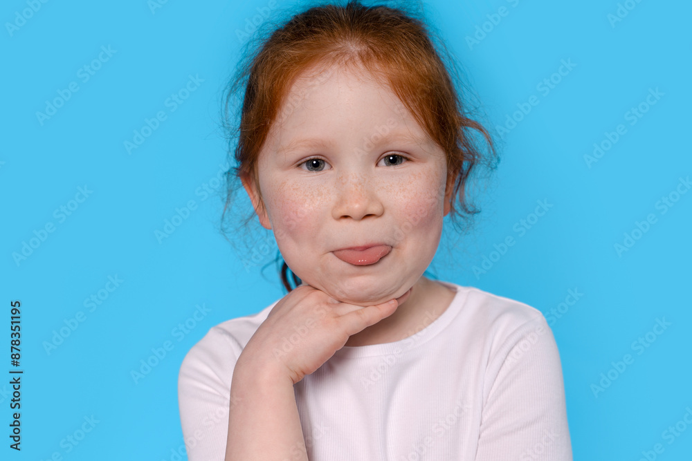 Young Redhead Girl Sticking Tongue Out In Front Of Blue Background