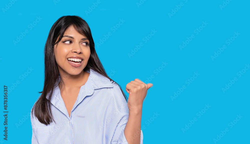 Woman In Striped Shirt Smiling and Pointing Right Against Blue Background with Copy Space Woman In Striped Shirt Smiling and Pointing Right Against Blue Background with Copy Space