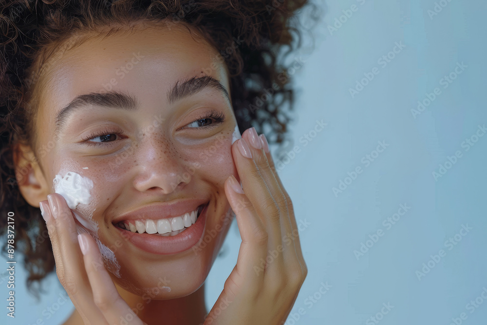 A woman is smiling and applying a white cream to her face