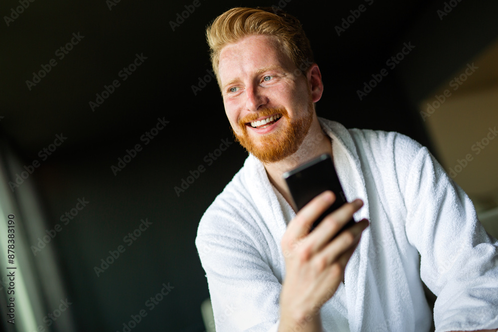 Happy smiling man relaxing while looking at mobile phone. Man reading news on smartphone Happy smiling man relaxing while looking at mobile phone. Man reading news on smartphone