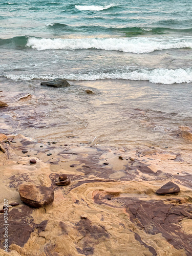 Teal blue water and waves on the orange rocks of the Pictured Lakes National Lakeshore photo