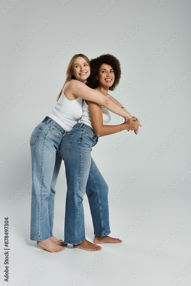 Two women in tank tops and jeans smile as they pose for the camera, with the woman on the left arm around the woman on the right Two women in tank tops and jeans smile as they pose for the camera, with the woman on the left arm around the woman on the right