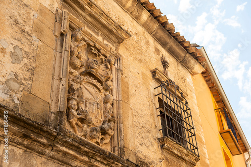 imagen de un escudo de piedra en una pared junto a una ventana de hierro 