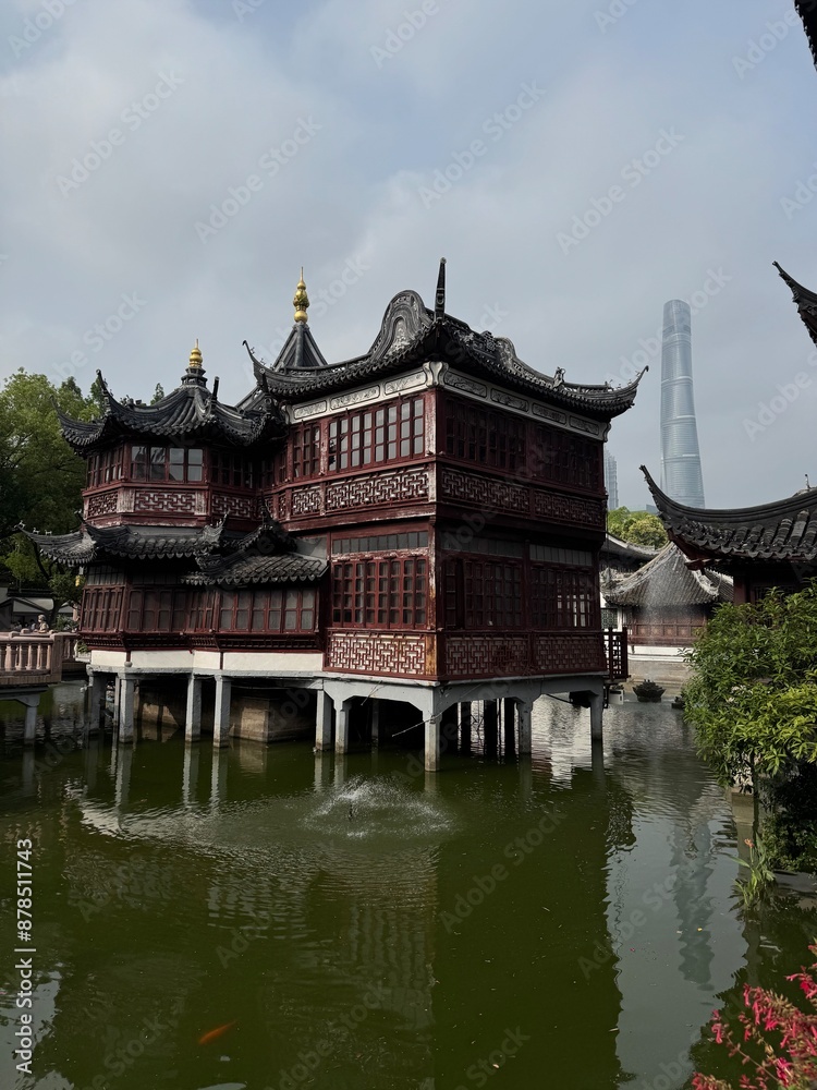 Fototapeta premium Historic Pavilion Overlooking Serene Pond at Yu Garden with Modern Shanghai Skyline in Background