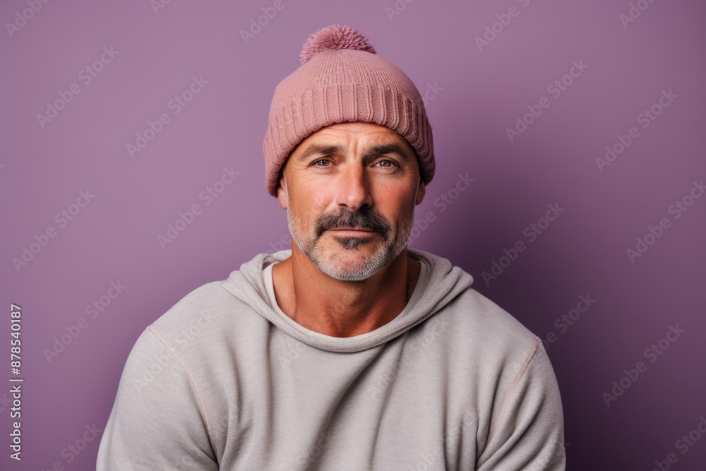 Portrait of a merry man in his 40s sporting a trendy beanie while standing against pastel or soft colors background
