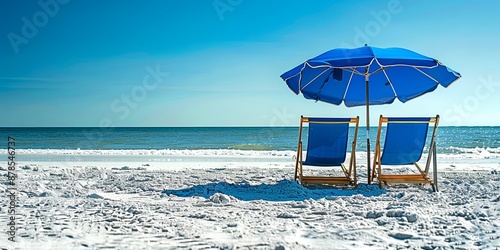 Two blue beach chairs under a blue umbrella on a white sandy beach.