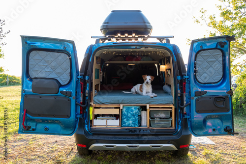 Mit kleinem Hund im Mini Van auf Reise, junger weißer Hund liegt auf dem Bett im Camper, Abenteuer auf vier Pfoten,  Hund genießt die Aussicht  photo