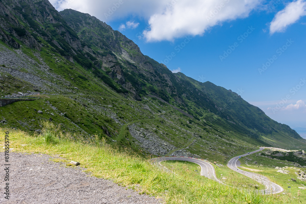A road winds through a grassy hillside with mountains in the background A road winds through a grassy hillside with mountains in the background