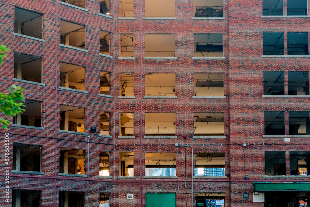 Apartment building under demolition with windows removed, leaving exposed brickwork and interiors and glimpse of modern replacement in background. Apartment building under demolition with windows removed, leaving exposed brickwork and interiors and glimpse of modern replacement in background.