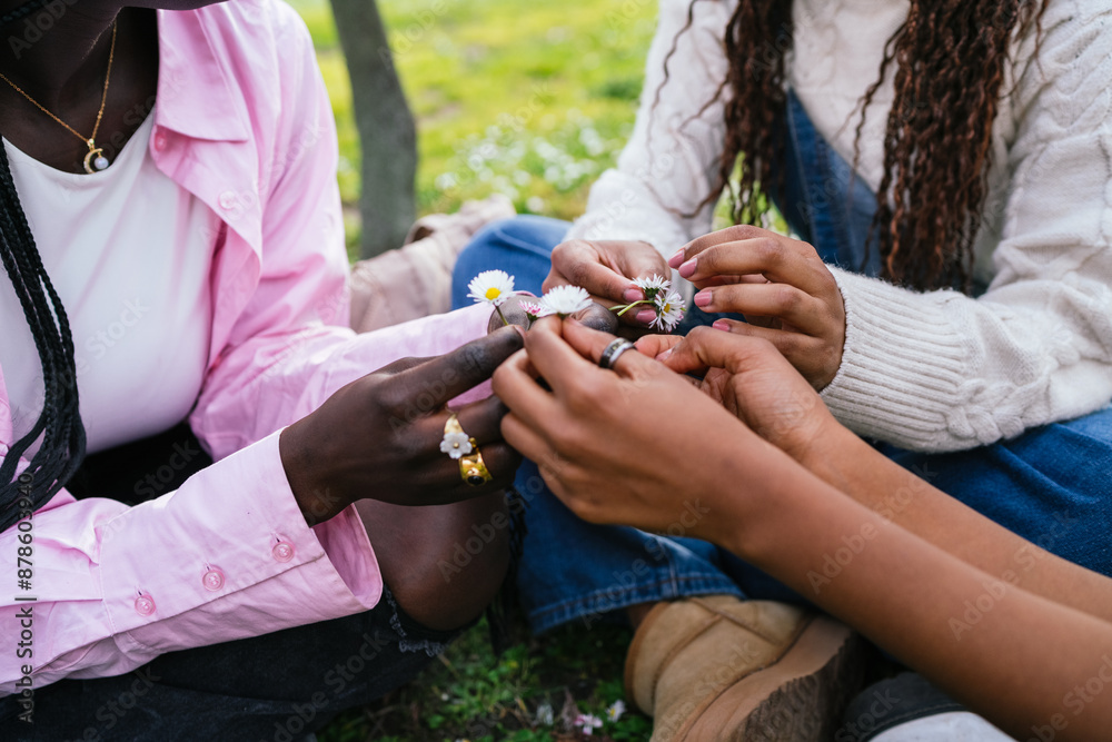 Hands of three African women picking flowers while sitting on the grass in a park. Hands of three African women picking flowers while sitting on the grass in a park.