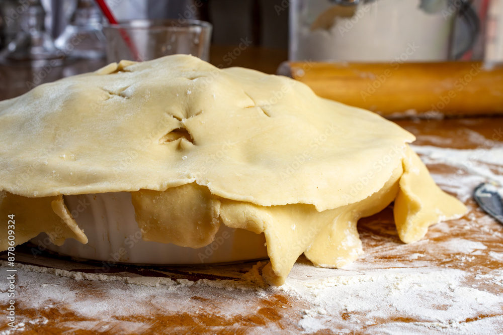 Making a pie: Top crust. Dough is unfolded with edges hanging over the side of the prepared apple pie. Making a pie: Top crust. Dough is unfolded with edges hanging over the side of the prepared apple pie.