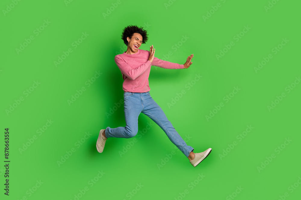 Full length photo of attractive funny guy wear pink sweater jumping high fighting emtpy space isolated green color background Full length photo of attractive funny guy wear pink sweater jumping high fighting emtpy space isolated green color background