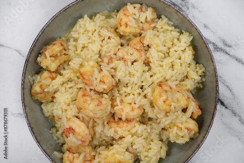 Seafood. Top view of a bowl with shrimps and rice with saffron on the white marble table