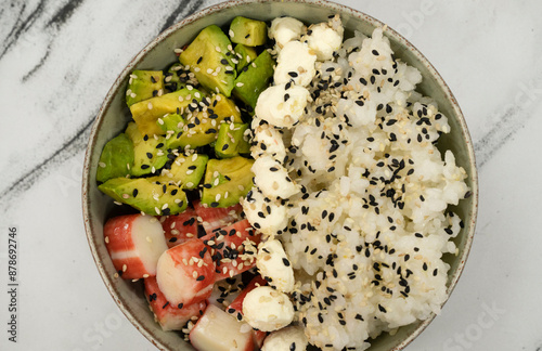 Top view of an asian seafood salad made with kani kama, avocado, sushi rice, cream cheese and sesame seeds, in a bowl on the white marble table