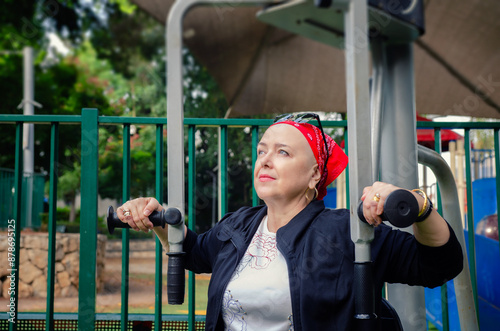 Mature woman is working out on the fitness machine. She has a bald head, indicating she is undergoing chemotherapy, a common treatment for cancer that often results in hair loss.