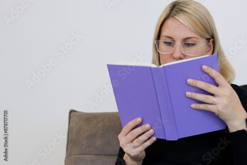 Close up portrait of a caucasian millennial female with glasses siting on a couch and reading a book © TatjanaMeininger