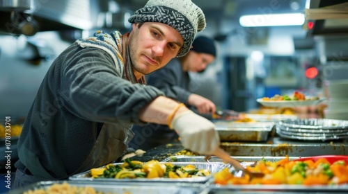 Young male volunteer serving food in busy kitchen setting photo