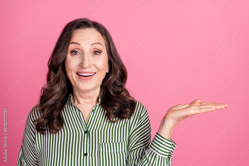 Photo of nice aged lady hold empty space wear striped shirt isolated on pink color background Photo of nice aged lady hold empty space wear striped shirt isolated on pink color background