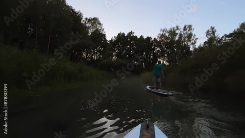 Active man standing on board with paddle water sport active movement at serpentine lake with greenery POV shot. Sportsman paddleboarding supsurfing at nature scenery photo