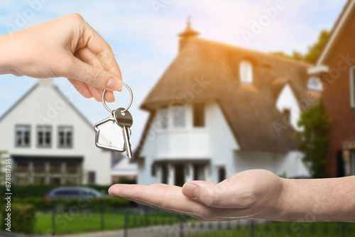 Real estate agent giving house key to new owner against beautiful dwelling, closeup photo