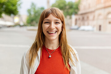 Happy young caucasian girl smiling at camera standing at city street. Outside portrait of joyful beautiful italian woman over urban background.