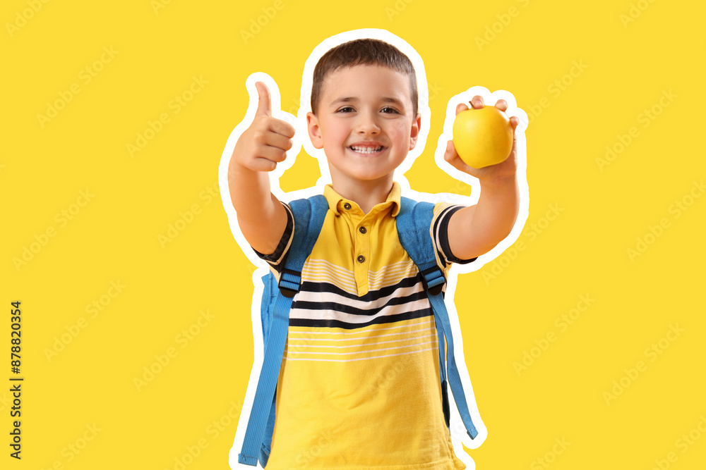 Little schoolboy with apple showing thumb-up on yellow background