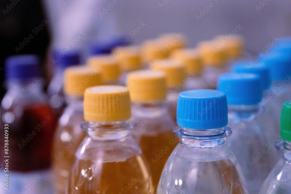 Many blue, yellow, green drinking water and refreshment beverage bottle caps and pure drinking water bottles in a drinking water production plant or supermarket shelf. Close up. Selective focus. Many blue, yellow, green drinking water and refreshment beverage bottle caps and pure drinking water bottles in a drinking water production plant or supermarket shelf. Close up. Selective focus.