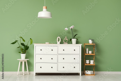 White chest of drawers with houseplant and shelving unit near green wall in room