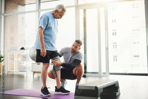 Senior, man and physiotherapist with knee bandage for support, circulation or compression for healing. Fitness, physiotherapy and elderly person with joint wrap, mobility training and exercise in gym