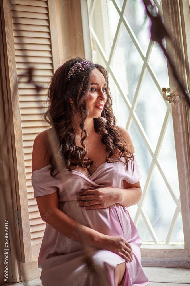 Fototapeta premium Portrait of a beautiful pregnant woman in a pink dress at home
