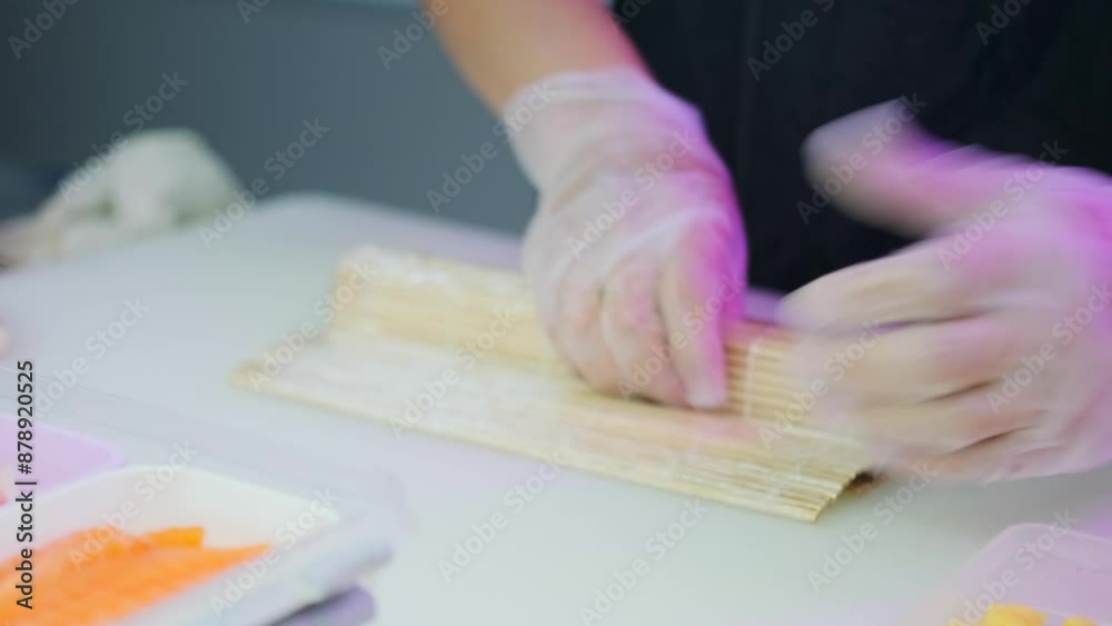 Sushi chef with hands in white rubber gloves making rolls using a special bamboo mat in table cafe kitchen. Close up. Sushi chef with hands in white rubber gloves making rolls using a special bamboo mat in table cafe kitchen. Close up.