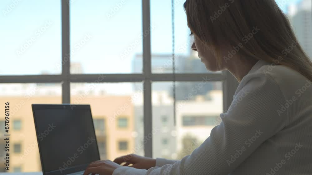 Generation Z woman working at desk in office next to large windows with view over the city Generation Z woman working at desk in office next to large windows with view over the city