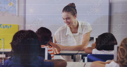 Image of graphs over caucasian female teacher and class of diverse pupils photo