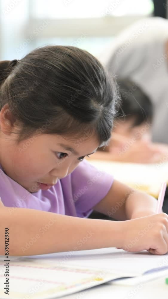 Vertical video of an elementary school girl looking up and copying the blackboard while studying and holding a pencil during an English class in a classroom. Vertical video of an elementary school girl looking up and copying the blackboard while studying and holding a pencil during an English class in a classroom.