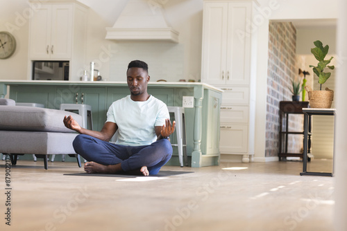 African american man practicing yoga meditation sitting on floor at home, copy space