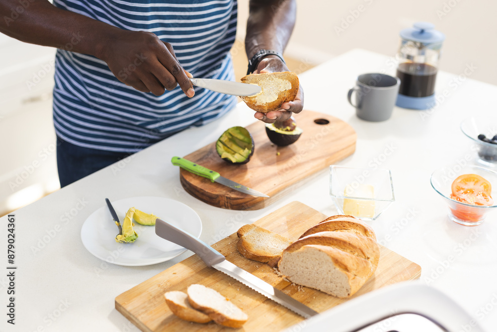 Midsection of african american man buttering toast to have with avocado in kitchen, copy space Midsection of african american man buttering toast to have with avocado in kitchen, copy space