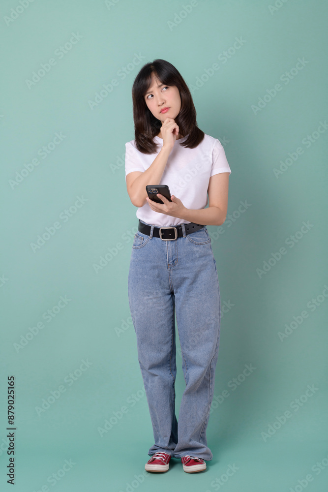 Woman holding phone with thoughtful expression, dressed in white t-shirt and jeans. Woman holding phone with thoughtful expression, dressed in white t-shirt and jeans.