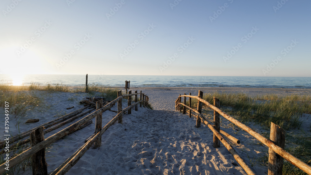Sandy entrance to the beach. Sunset. Wooden balustrades. Footprints in the sand. Dunes covered with grass. Slajszewo, Poland. Baltic Sea