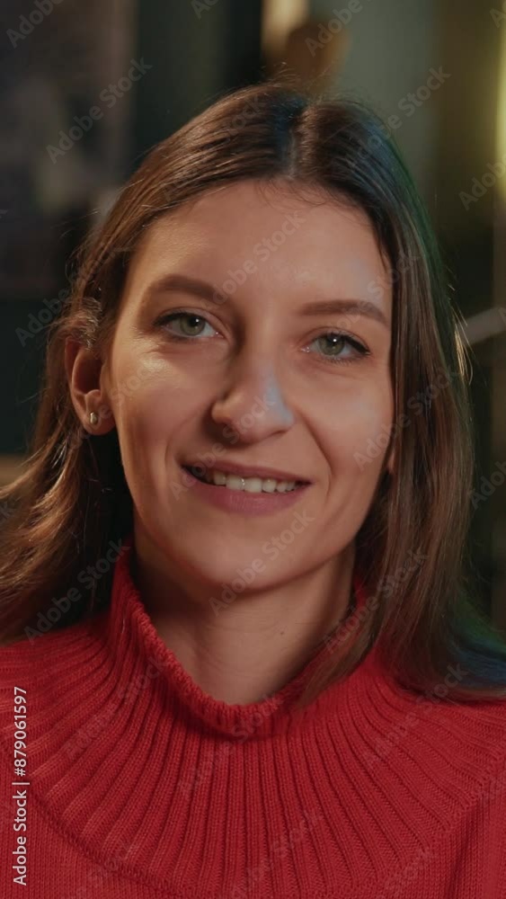 Closeup portrait of good-looking brown-haired young woman in coral sweater with green eyes looking at camera. Smiling girl sitting on couch in living room in evening. Blurred background. Indoors Closeup portrait of good-looking brown-haired young woman in coral sweater with green eyes looking at camera. Smiling girl sitting on couch in living room in evening. Blurred background. Indoors